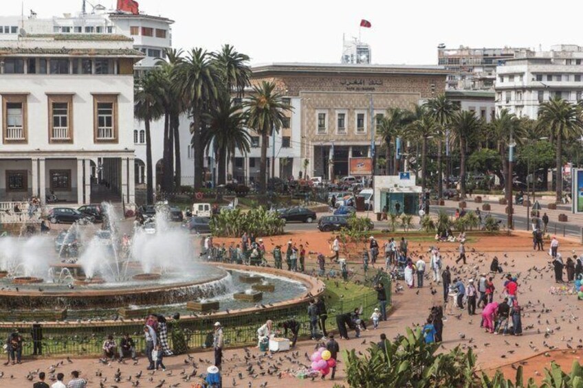A public square with a fountain, palm trees, and people. 5