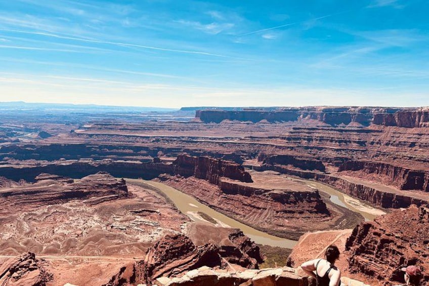A canyon landscape with layered rock formations, a winding river, and a person standing on a cliff. 4
