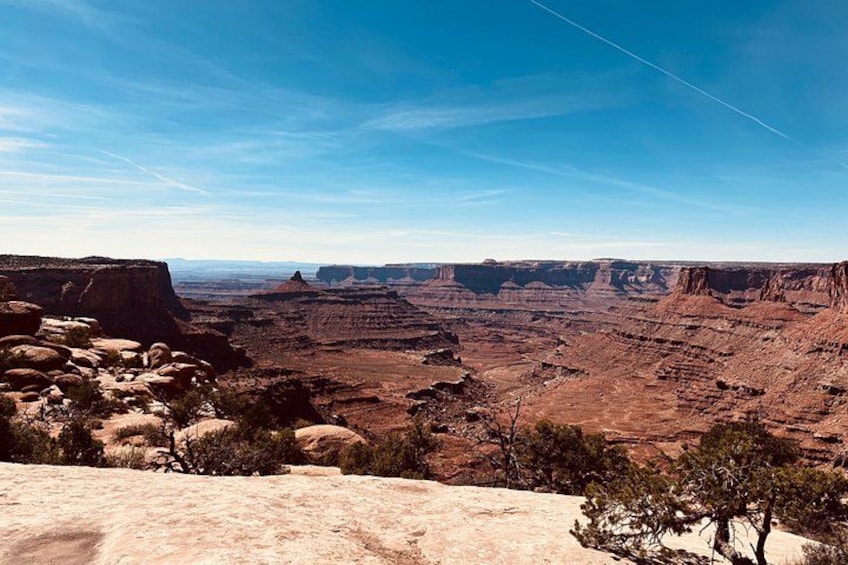 A canyon landscape with layered rock formations, sparse vegetation, and a clear sky. 5