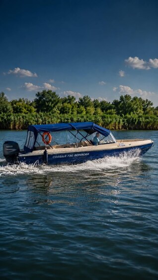 A blue boat with a canopy, named 'Corsar 730 Bowrider,' moving on water with a forested shoreline in the background. 5