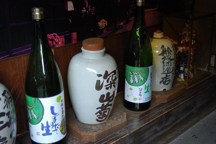 A shelf with various bottles and a ceramic jar, some with Japanese characters. 4
