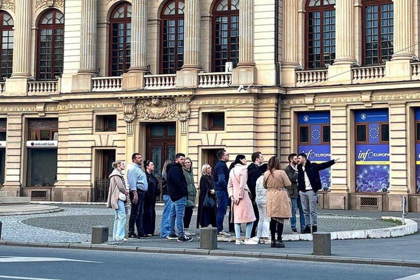 A group of people standing on a sidewalk in front of a building with large windows and a European Union flag. 3