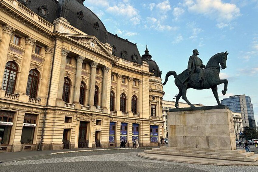 Un edificio storico dall'architettura classica, una statua di un uomo a cavallo e una strada acciottolata. 5