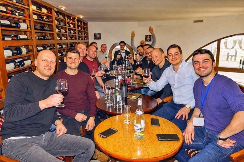 Un gruppo di persone sedute attorno a un tavolo rotondo in una cantina, con bicchieri di vino in mano. 1