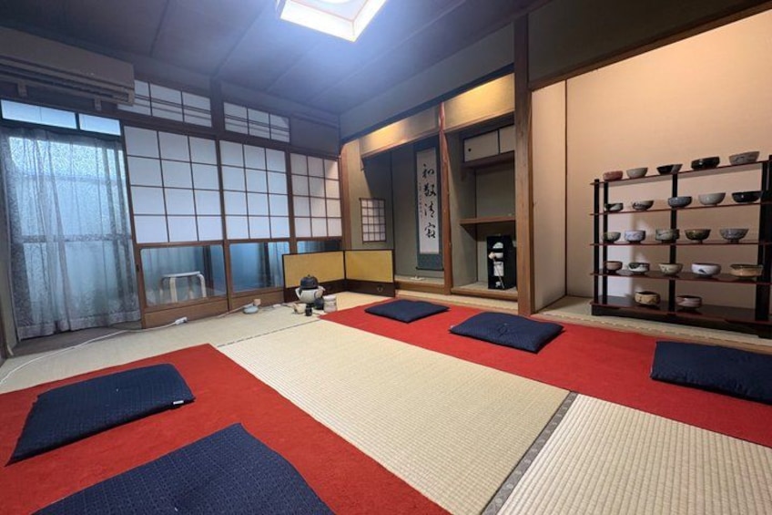 A traditional Japanese room with tatami mats, a tea set, and a shelf with bowls. 3