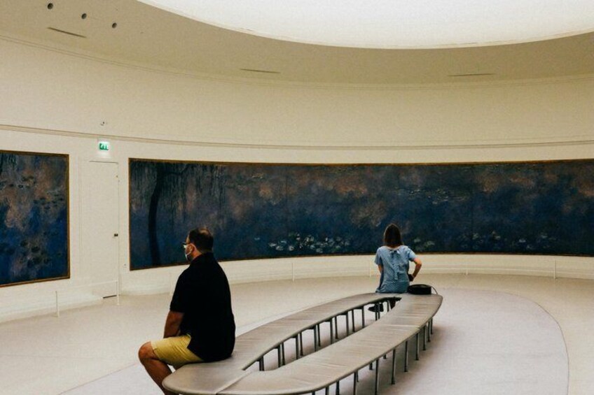 Eine Kunstgalerie im Innenbereich mit abstrakten Gemälden an den Wänden und einer gebogenen Sitzbank. 5