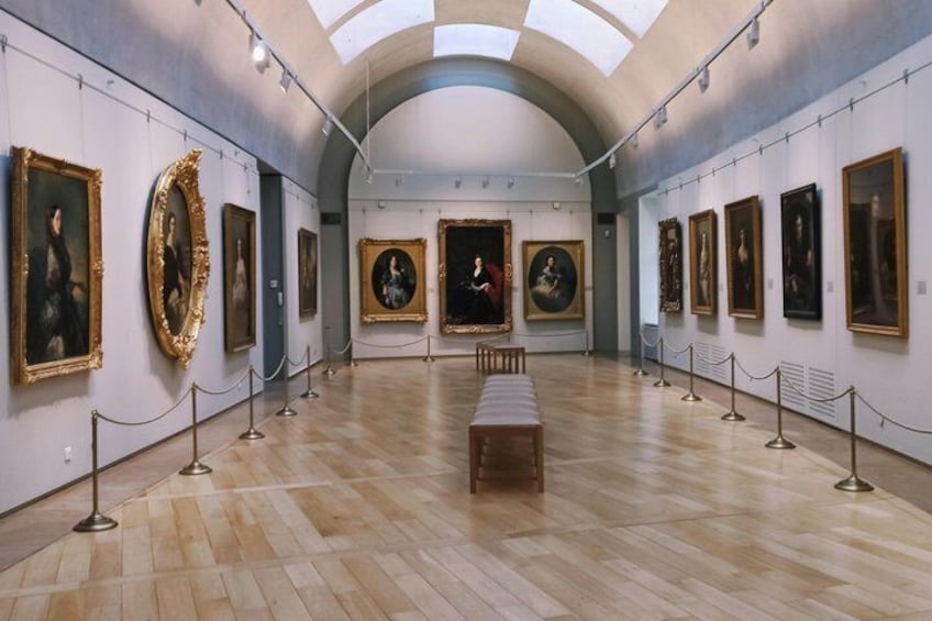 Eine Kunstgalerie mit gerahmten Gemälden an den Wänden und einer hölzernen Bank in der Mitte. 4