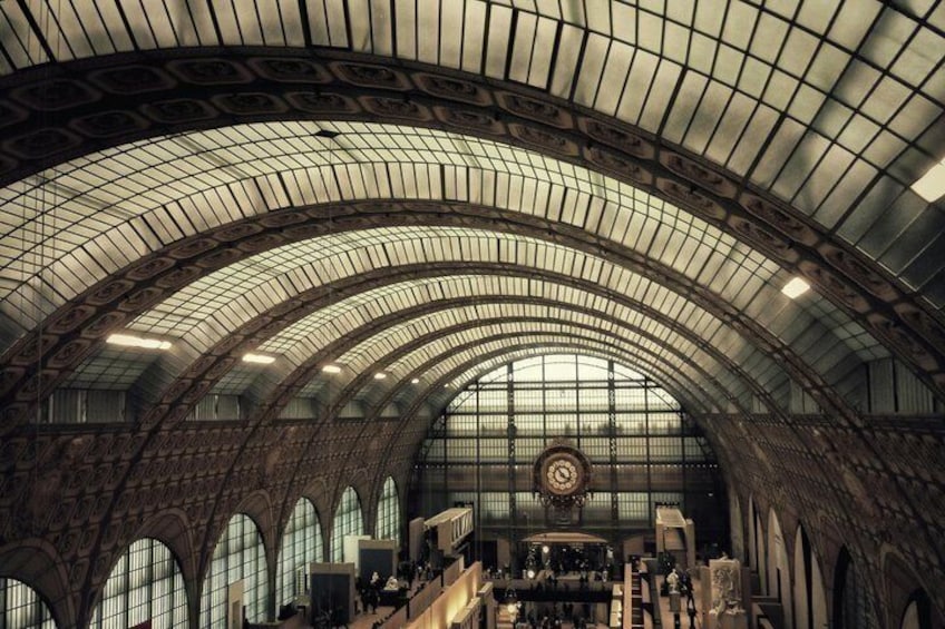 Eine gewölbte Decke mit einer Uhr, großen Fenstern und einem zentralen, offenen Bereich in einem Bahnhof. 1