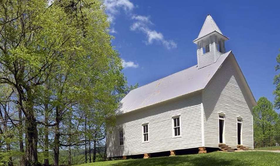 A white church with a steeple, surrounded by trees and grass. 2