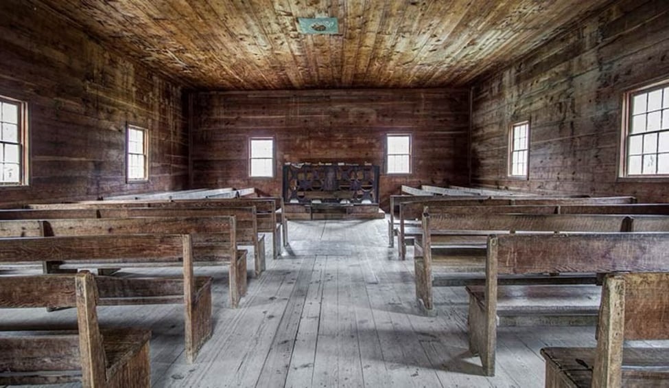 An interior with wooden benches arranged in rows, a wooden floor, and a rustic ceiling. 3
