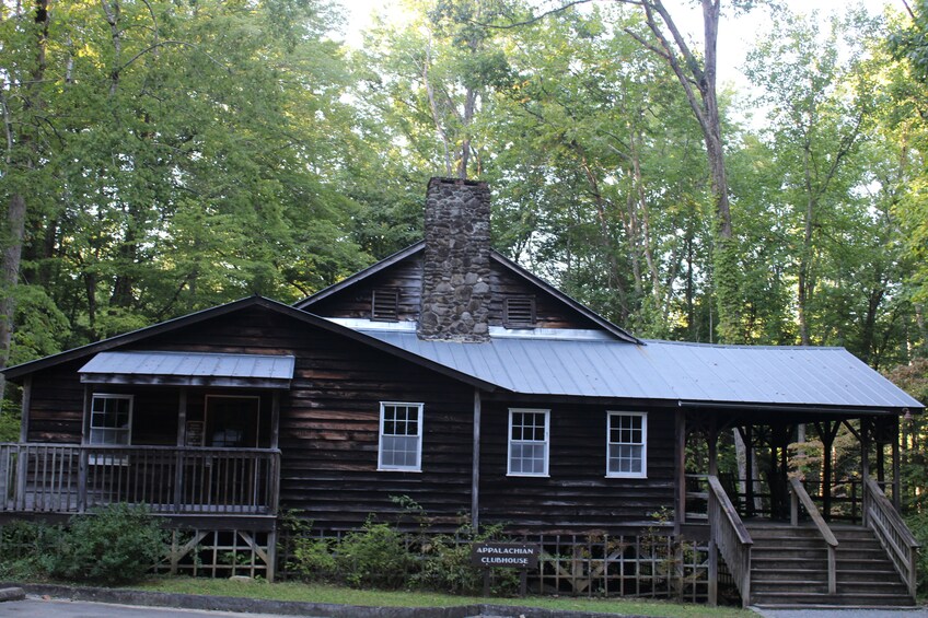 A rustic Appalachian Clubhouse with a stone chimney, wooden deck, and a staircase leading to the entrance. 3