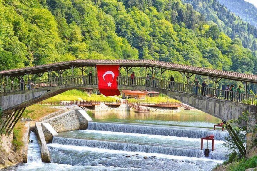 A bridge over a waterfall with a flag, surrounded by lush greenery. 2