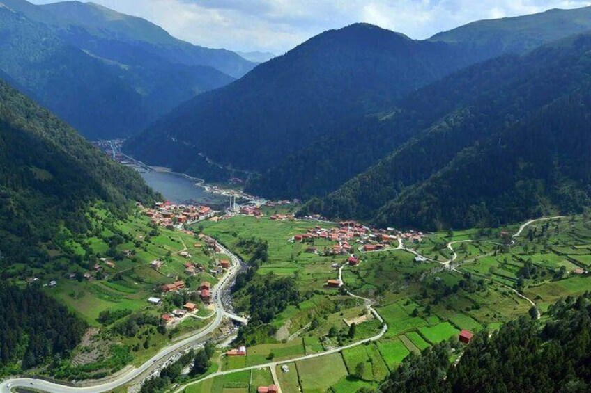 A mountainous landscape with a winding road, a small village, and a lake. 5