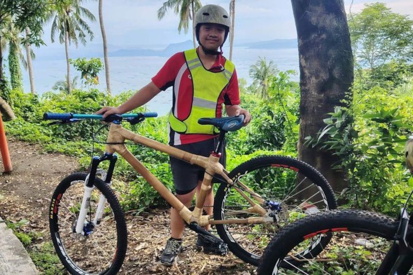 A person standing next to a mountain bike on a dirt path with a scenic view of the ocean and palm trees in the background. 4
