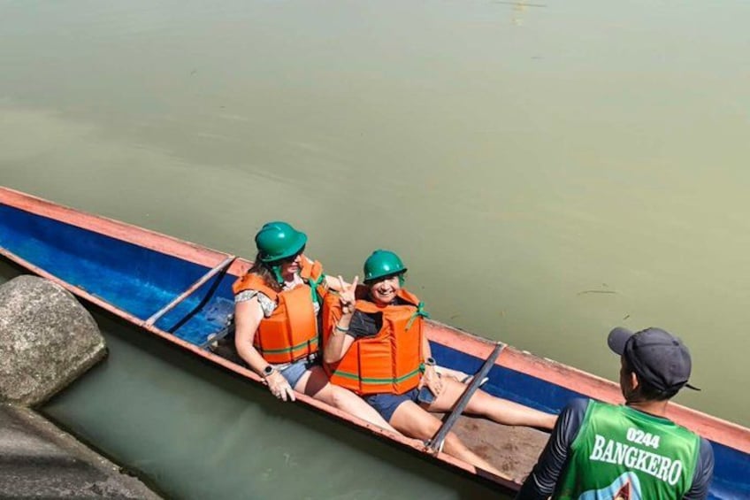Un canoë avec deux personnes portant des gilets de sauvetage et des casques, un guide vêtu d’un gilet vert, et une eau calme. 5