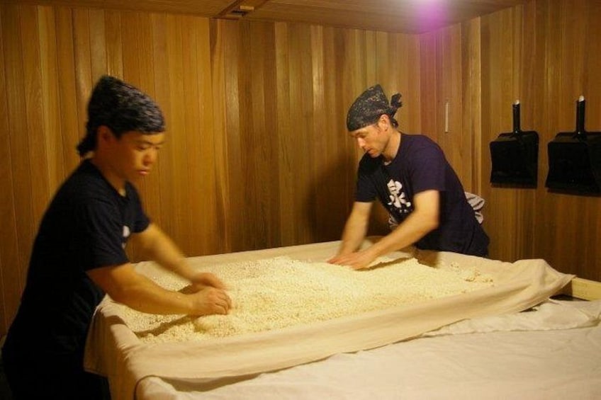 Two individuals working with a large pile of rice in a wooden room. 2