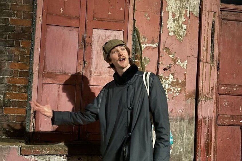 A person in a dark coat and hat standing in front of a weathered red door. 1