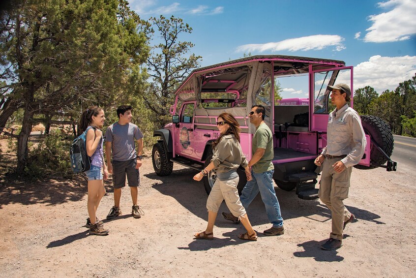 A group of people walking near a pink off-road vehicle in a desert-like setting with sparse vegetation. 2