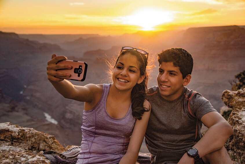 Two people taking a selfie on a mountain with a sunset in the background. 1