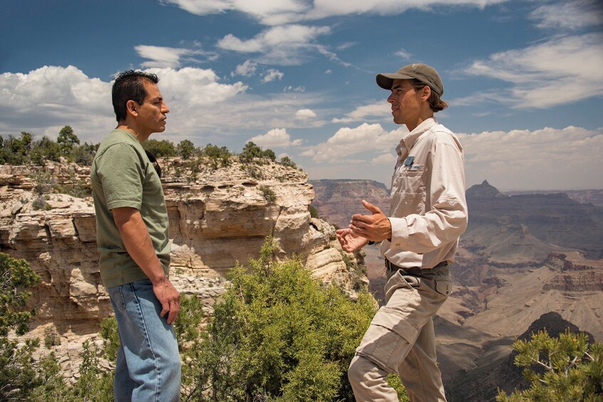 Two people conversing in a rocky canyon with a vast landscape in the background. 3