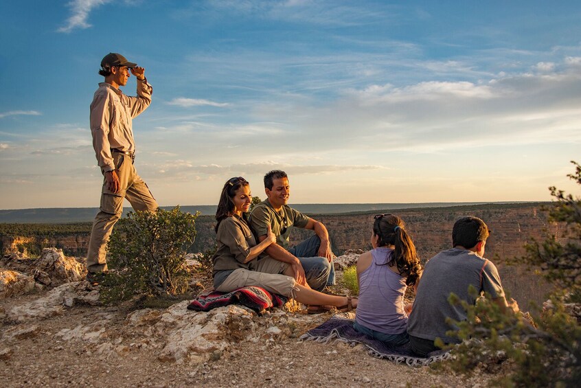 A group of people sitting on a rocky outcrop with a canyon in the background. 5