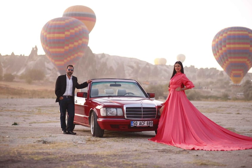 A red car, a woman in a pink dress, and hot air balloons in a rocky landscape. 2