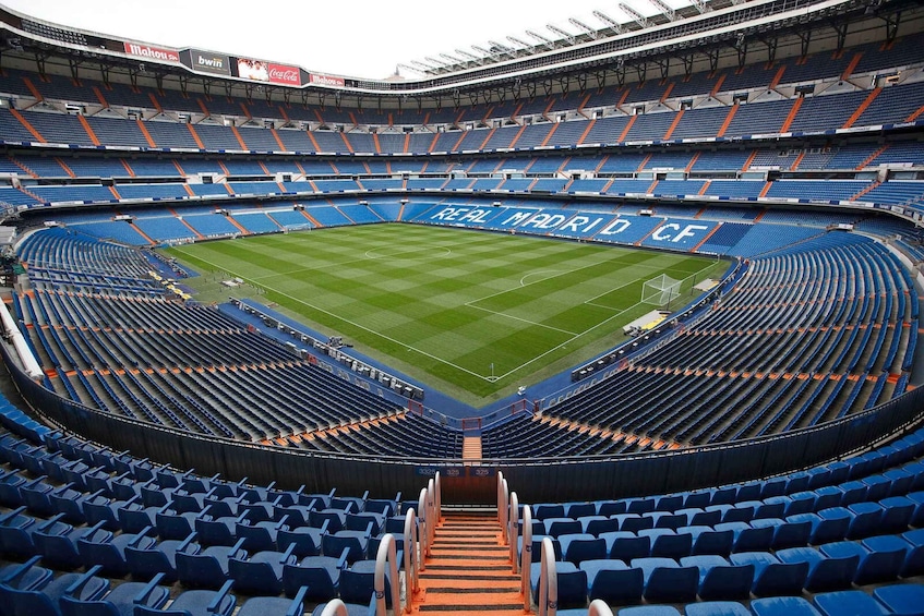 A stadium with blue seats and a green field, featuring 'Real Madrid CF' text. 3
