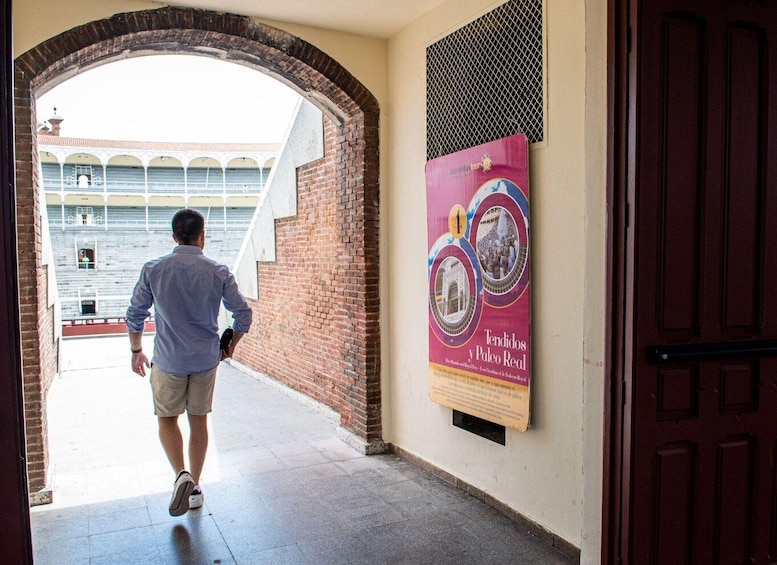 A man walking through a doorway towards a building with a red door and a poster on the wall. 2