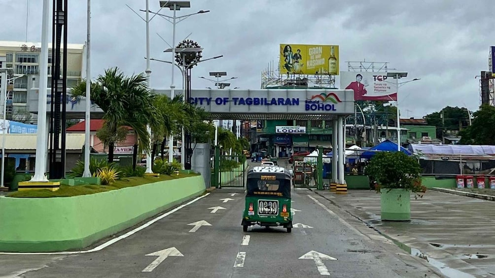 A tuk-tuk driving through a toll plaza with a sign for the City of Tagbilaran and a BP gas station. 5