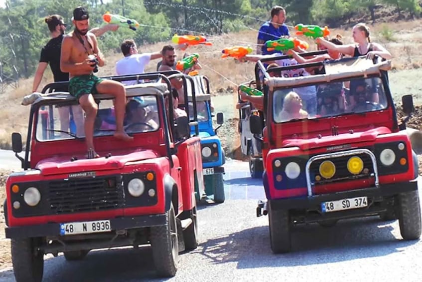 A convoy of red and blue off-road vehicles with passengers holding water guns. 3