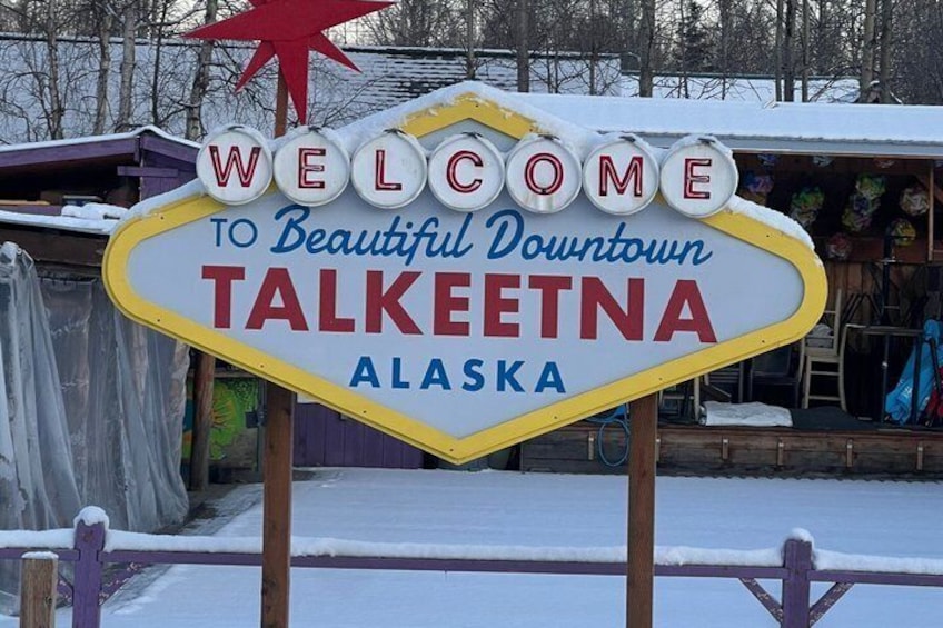 A welcome sign for Talkeetna, Alaska, with a red star and snow-covered ground. 1