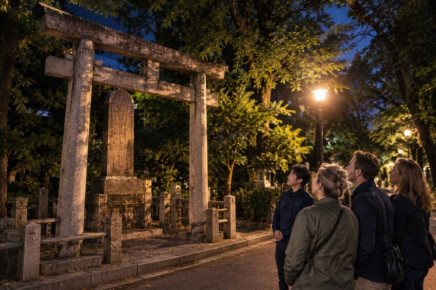 Puistossa sijaitseva kivinen torii-portti hämärän aikaan, ja sen lähellä on ihmisiä. 5