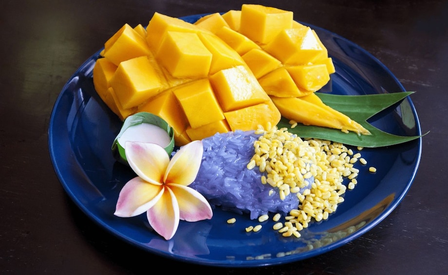 A plate with yellow mango chunks, purple rice, yellow beans, a flower, and a green leaf. 3