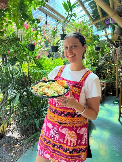 A person holding a plate of food in a greenhouse with various plants and hanging pots. 4