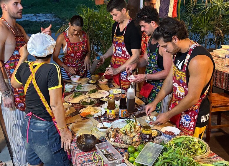 A group of people preparing food outdoors with a variety of ingredients and utensils on a table. 3
