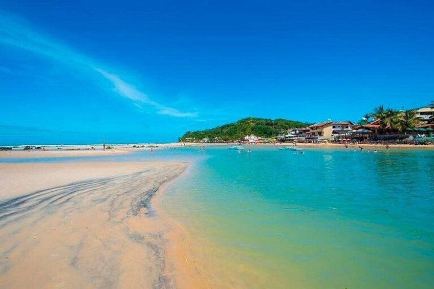 Una spiaggia con acque cristalline turchesi, una riva sabbiosa e edifici sullo sfondo. 2