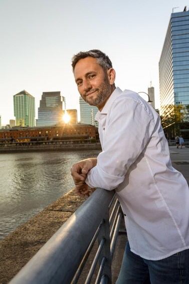 A man leaning on a railing by a river with a cityscape in the background. 2