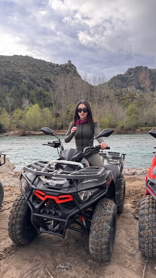 A person on an ATV near a river with a mountainous backdrop. 2