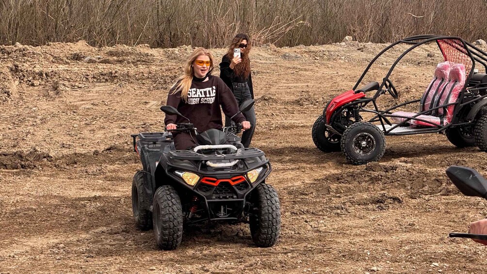 A person riding an ATV on a dirt path with a red vehicle in the background. 5