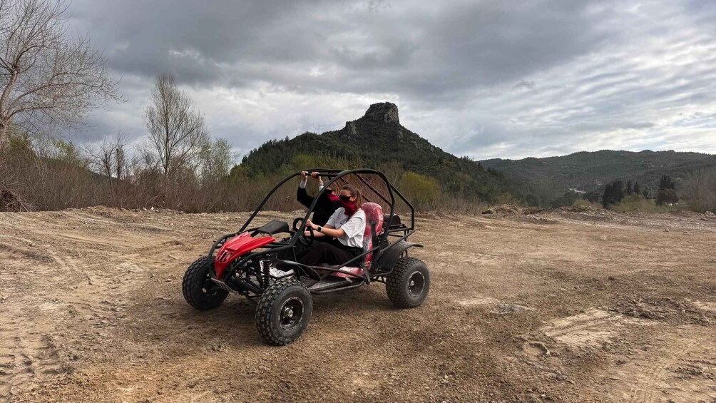 A person in a red off-road vehicle on a dirt path with a mountain in the background. 4