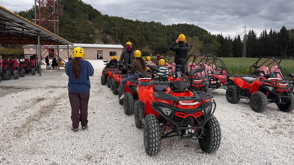 A group of people on ATVs with helmets, parked on gravel with a building and trees in the background. 5