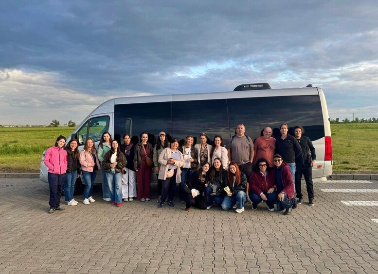 A group of people posing in front of a white van on a paved area with grass fields in the background. 4
