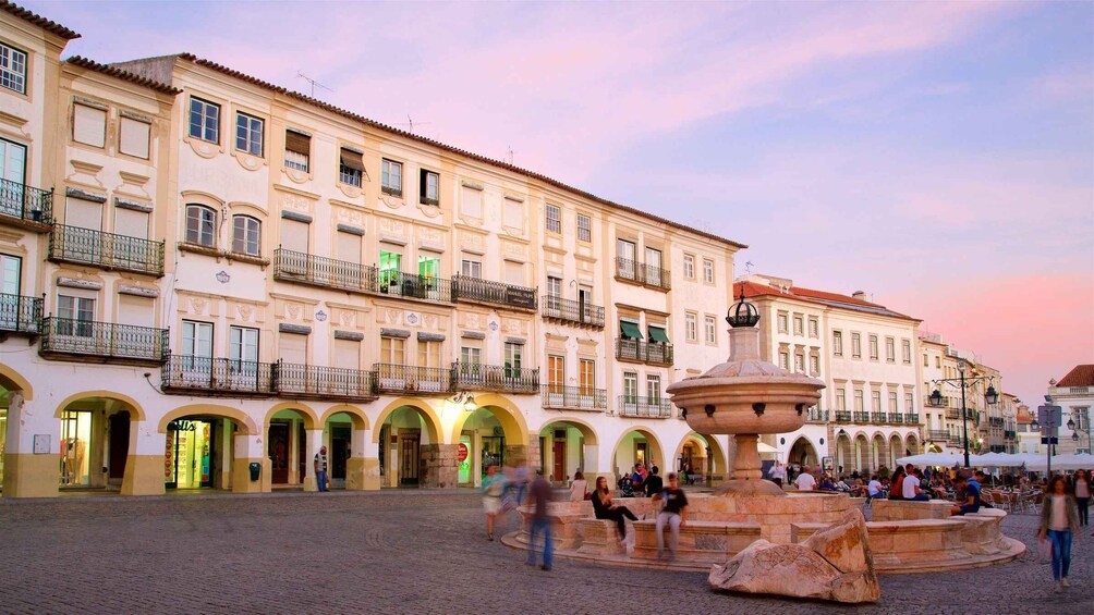 A historic square with a central fountain, surrounded by buildings with balconies and arched doorways. 2