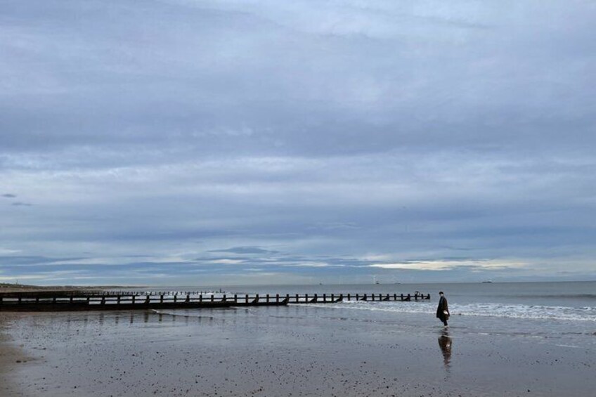 A wet beach with a wooden pier extending into the water and a person walking along the shore. 5