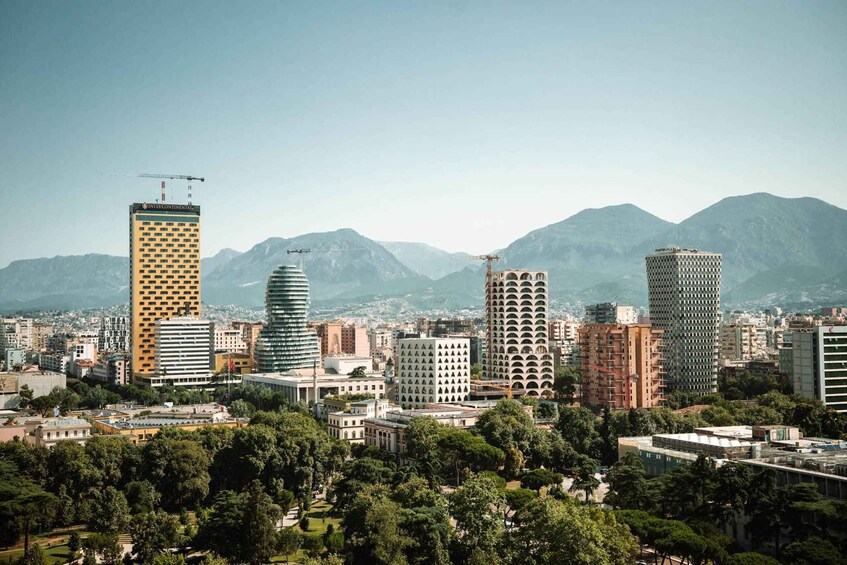 A cityscape with a prominent yellow building, a construction crane, and mountains in the background. 3