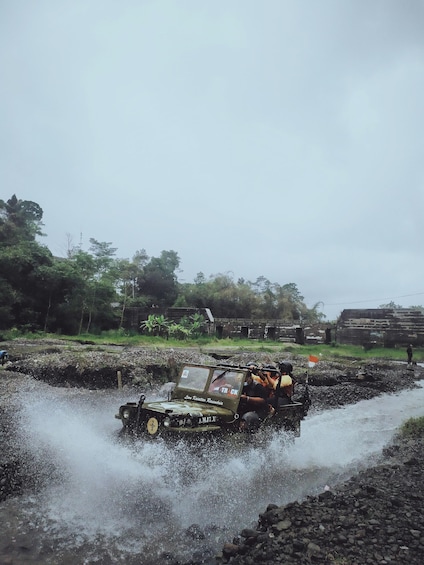 A vehicle driving through a shallow water crossing, surrounded by greenery and a stone wall. 2