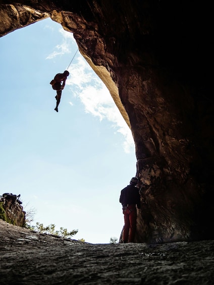 A person rappelling down a rock face with a guide above. 1