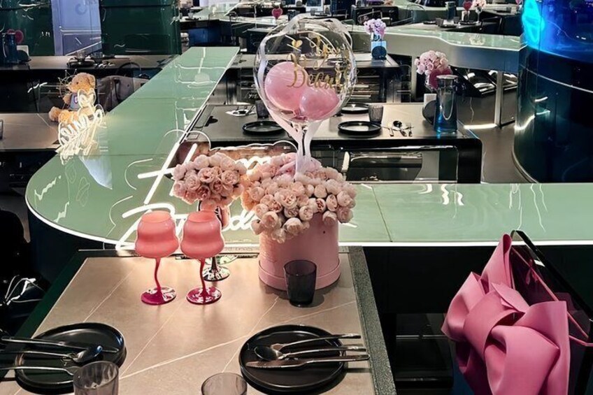 Een restaurantinterieur met gedekte tafels, roze bloemdecoraties en een neonbord. 2
