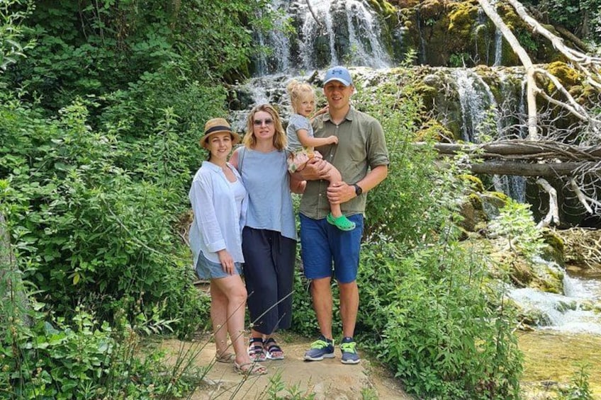 Une famille de quatre personnes se tient dans un jardin luxuriant, avec une cascade en arrière-plan. 3