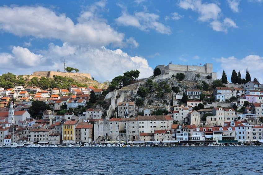 A coastal town with colorful buildings, a prominent hilltop fortress, and a body of water in the foreground. 4